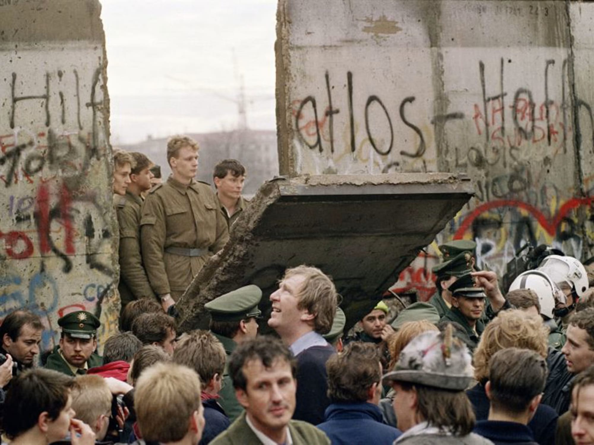 November, 1989: A group of men in military fatigues look through a breach in the Berlin wall at a joyous crowd.